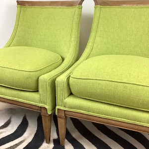 May include: Two lime green armchairs with wooden frames and legs. The chairs have a curved back and a rounded seat cushion. The wooden trim is a medium brown color. The chairs are placed on a black and white zebra-striped rug.