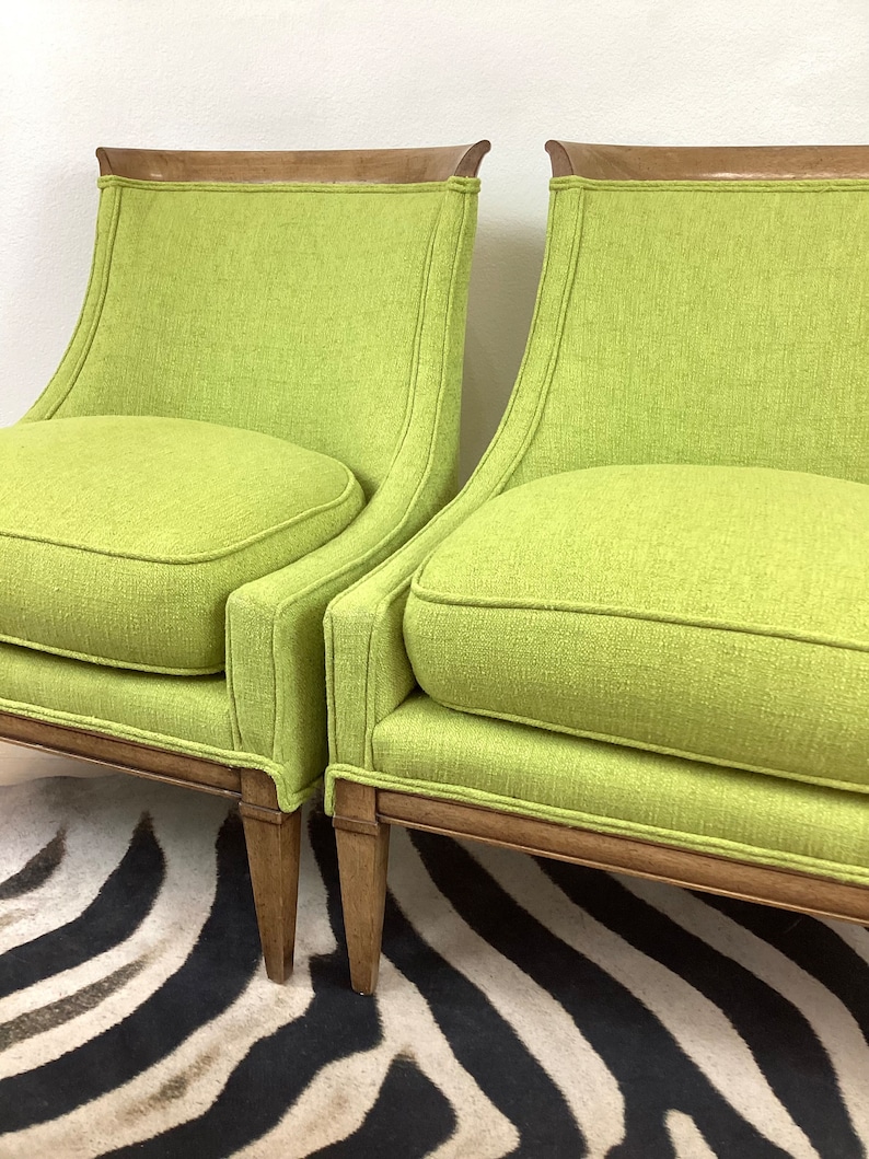 May include: Two lime green armchairs with wooden frames and legs. The chairs have a curved back and a rounded seat cushion. The wooden trim is a medium brown color. The chairs are placed on a black and white zebra-striped rug.