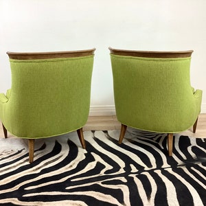 May include: Two mid-century modern armchairs with a vibrant green fabric upholstery. The chairs have a curved back design, wooden legs, and a dark wood trim along the top. They are set on a zebra-striped rug.