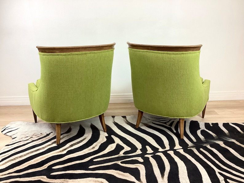 May include: Two mid-century modern armchairs with a vibrant green fabric upholstery. The chairs have a curved back design, wooden legs, and a dark wood trim along the top. They are set on a zebra-striped rug.