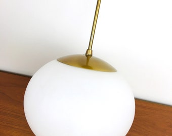May include: A white globe pendant light with a brass finish. The light is hanging from a single brass rod.