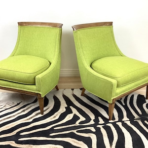 May include: Two lime green upholstered armchairs with wooden frames and legs. The chairs have a curved back and a square seat cushion. The chairs are placed on a zebra-print rug.