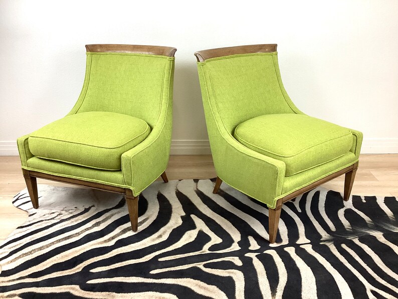 May include: Two lime green upholstered armchairs with wooden frames and legs. The chairs have a curved back and a square seat cushion. The chairs are placed on a zebra-print rug.