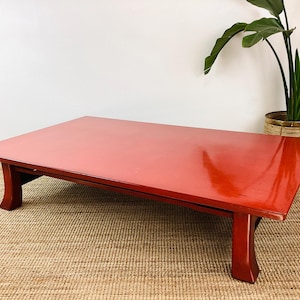 May include: A red lacquered coffee table with a rectangular top and four legs. The table is made of wood and has a glossy finish.