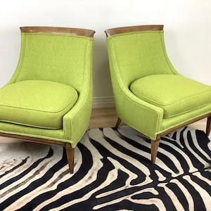 May include: Two lime green upholstered armchairs with wooden frames and a dark wood accent at the top of the backrests. The chairs have a curved back and seat cushions. The chairs are on a zebra print rug.