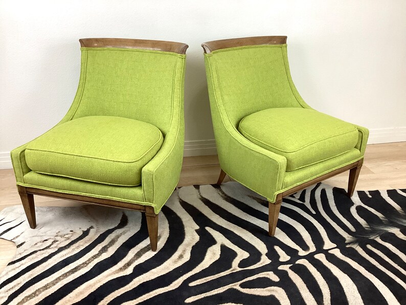 May include: Two lime green upholstered armchairs with wooden frames and a dark wood accent at the top of the backrests. The chairs have a curved back and seat cushions. The chairs are on a zebra print rug.