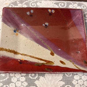May include: Rectangular ceramic serving dish with a unique color scheme. The dish features a diagonal split with a cream-colored section and a deep red section. A purple stripe divides the two sections. The dish is decorated with small blue and gold accents.