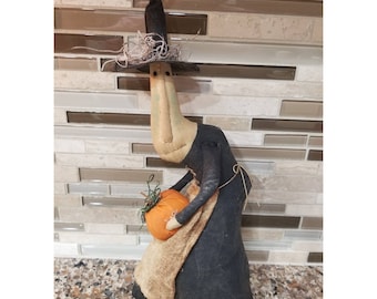 May include: A handmade witch doll with a black pointed hat, holding an orange pumpkin. The doll is wearing a black dress with a brown apron and has a simple face.