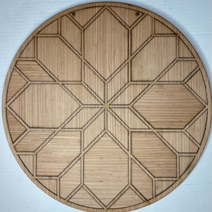 May include: A round wooden wall decor with a geometric design. The design is made up of multiple overlapping hexagons and triangles, creating a starburst pattern. The wood is a light brown color.