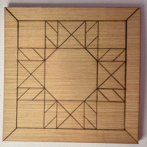 May include: A square wooden board with a geometric design. The board has a light brown wood grain finish. The design consists of a central circle surrounded by angular shapes and lines, all in black. The board is framed by a black border.