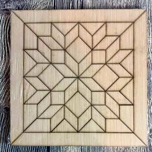 May include: A square wooden craft piece with a geometric starburst design. The design is composed of various diamond and square shapes, with dark lines outlining each shape. The wood has a light, natural color.