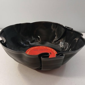 May include: A black bowl crafted from a repurposed vinyl record with a wavy, folded edge. The center of the bowl features a circular red Columbia record label with the text Bruce Springsteen and Born in the U.S.A. printed in black ink.