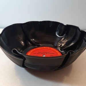 May include: A black, upcycled vinyl record bowl. The bowl is made from a repurposed record, with the original label visible in the center. The label is red with white text that reads "Neil Diamond You Don't Bring Me Flowers".