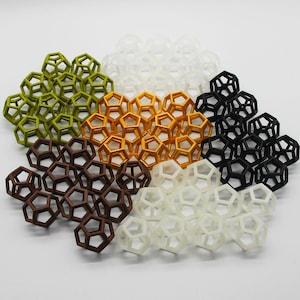 Op de afbeelding: Een verzameling van zes geometrische vormen gemaakt van plastic in verschillende kleuren, waaronder groen, bruin, goud, wit en zwart. De vormen zijn in een cirkel op een witte achtergrond gerangschikt.