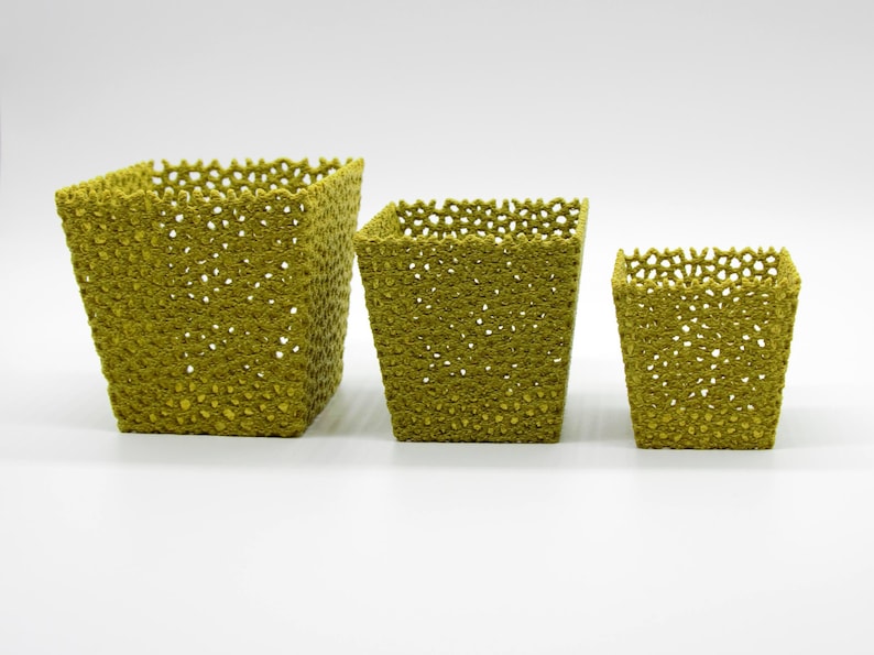 May include: Three olive-green, square-shaped baskets of varying sizes. The baskets have a textured, open-weave design with small holes throughout. The largest basket is approximately 7 inches tall, the medium is 5 inches, and the smallest is 3 inches.