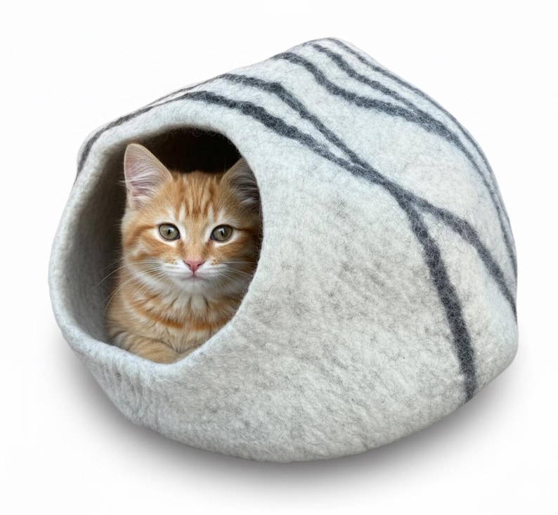 May include: A small orange tabby cat peeks out from a gray and white striped cat bed. The bed is a rounded, cave-like structure made of felted material, providing a cozy and enclosed space for the cat to rest.