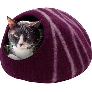 May include: A dark purple cat bed with white stripes, shaped like a dome. A black and white cat is inside the bed, looking out. The bed is made of a soft, felt-like material, providing a cozy space for a pet.