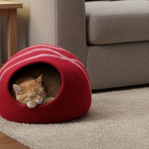 May include: A red cat bed with white stripes, shaped like a dome, sits on a neutral-colored rug. An orange tabby cat is curled up inside the bed, sleeping peacefully. The bed is near a wooden side table and a gray sofa.