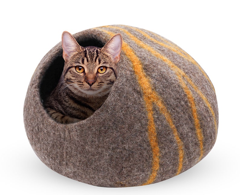 May include: A brown tabby cat inside a gray felted cat cave with orange stripes. The cat is looking directly at the viewer. The cat cave is a rounded shape, providing a cozy and enclosed space for the cat to rest.
