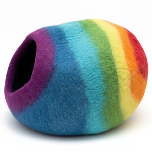 May include: A colorful, rainbow-striped pet bed. The bed is a rounded shape with an opening on one side. The colors include purple, blue, green, yellow, orange, and red. The bed is made of a felted material.