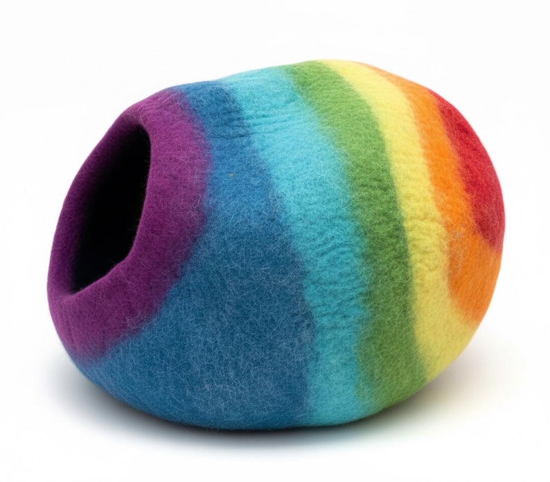 May include: A colorful, rainbow-striped pet bed. The bed is a rounded shape with an opening on one side. The colors include purple, blue, green, yellow, orange, and red. The bed is made of a felted material.