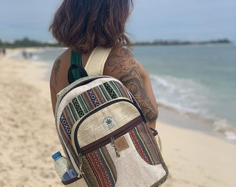 May include: A white hemp backpack with colorful woven patterns and a brown leather zipper pull. The backpack has a large main compartment and a smaller front pocket. The backpack is decorated with a green leaf logo that says "Hemp Leaf".