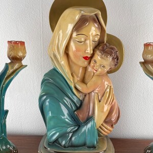 Peut inclure: Une statue vintage de la Vierge Marie tenant l'enfant J&eacute;sus. La statue est en pl&acirc;tre et peinte dans des tons de bleu, or et rose. La statue est sur une surface en bois.