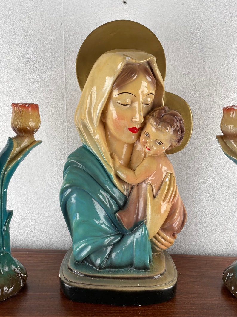 Peut inclure: Une statue vintage de la Vierge Marie tenant l'enfant J&eacute;sus. La statue est en pl&acirc;tre et peinte dans des tons de bleu, or et rose. La statue est sur une surface en bois.