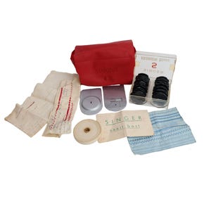 Peut inclure: Un kit d'accessoires pour machine à coudre Singer comprenant un sac de rangement rouge, une boîte en plastique transparent avec des disques noirs, deux plaques métalliques argentées, un ruban blanc et des échantillons de tissu cousus.