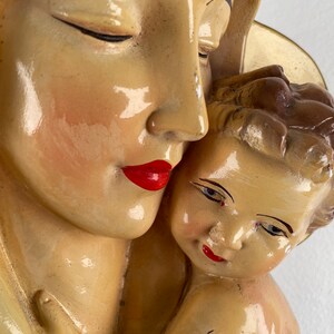 Peut inclure: Une sculpture en pl&acirc;tre vintage de la Vierge Marie tenant un b&eacute;b&eacute; J&eacute;sus. La sculpture est peinte en cr&egrave;me avec des l&egrave;vres rouges et des cheveux bruns. La sculpture est en gros plan.