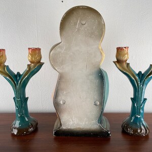 Peut inclure: Trois bougeoirs d&eacute;coratifs avec un motif de tulipe. Les bougeoirs sont en c&eacute;ramique peinte et ont un sch&eacute;ma de couleurs bleu sarcelle et jaune. Le bougeoir central est plus grand et pr&eacute;sente une figure peinte.