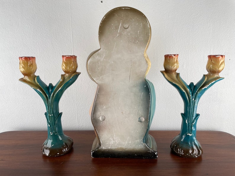 Peut inclure: Trois bougeoirs d&eacute;coratifs avec un motif de tulipe. Les bougeoirs sont en c&eacute;ramique peinte et ont un sch&eacute;ma de couleurs bleu sarcelle et jaune. Le bougeoir central est plus grand et pr&eacute;sente une figure peinte.