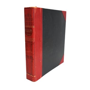 May include: An antique photo album with a red spine and corners, and a black cover. The spine features gold embossed text and decorative floral patterns. The album is slightly worn, suggesting its age and use.
