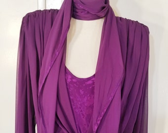 May include: A long-sleeved purple dress with a matching purple scarf. The dress has a scoop neckline and a flowing silhouette.