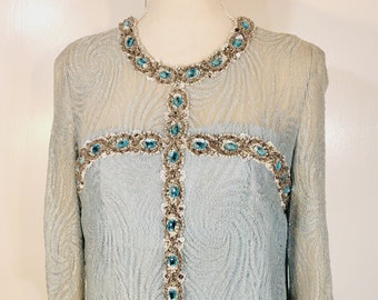 May include: A light blue dress with a long sleeve and a cross-shaped design made of silver and blue sequins.