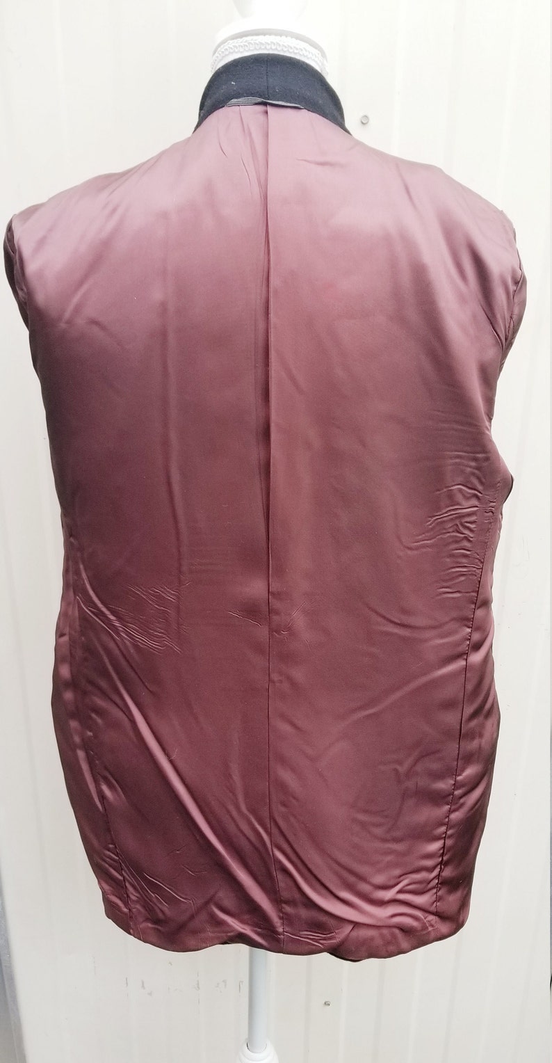 May include: Back view of a dark navy blazer with a black collar. The inside lining is a deep burgundy color, with a smooth, satin-like texture. The blazer is displayed on a white mannequin.