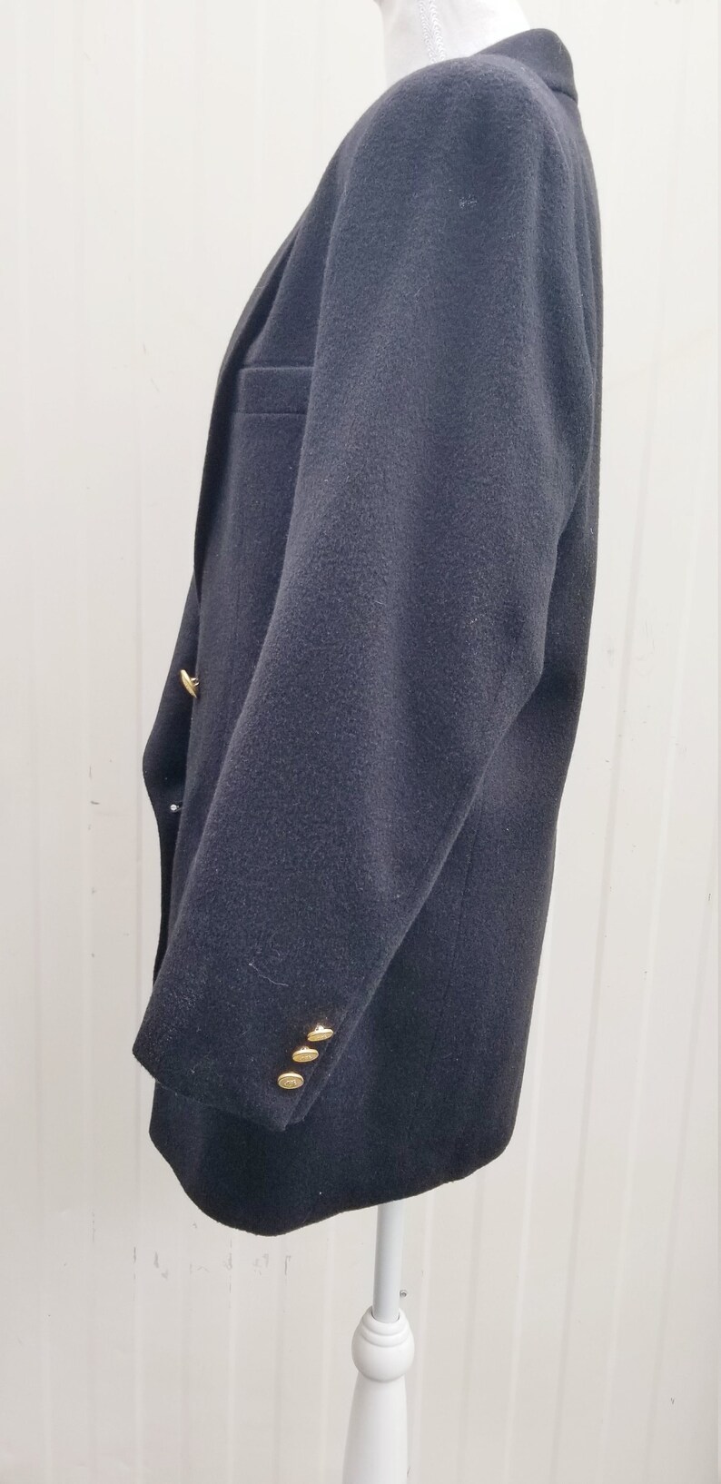 May include: A dark navy blazer with gold-colored buttons. The blazer has a classic design with a notched lapel and a tailored fit. The sleeves have three buttons. The blazer is displayed on a white mannequin.