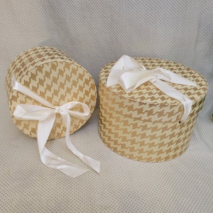 May include: Two round gift boxes with gold and white houndstooth patterns and white satin ribbon bows.