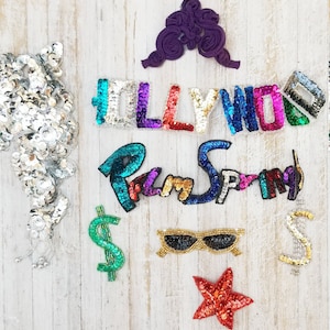 Puede incluir: Surtido de parches de lentejuelas de colores, incluyendo las palabras "HOLLYWOOD" y "Palm Springs", un signo de dólar, gafas de sol y una estrella.