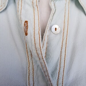May include: A light blue button-up shirt with a white button and brown stitching.