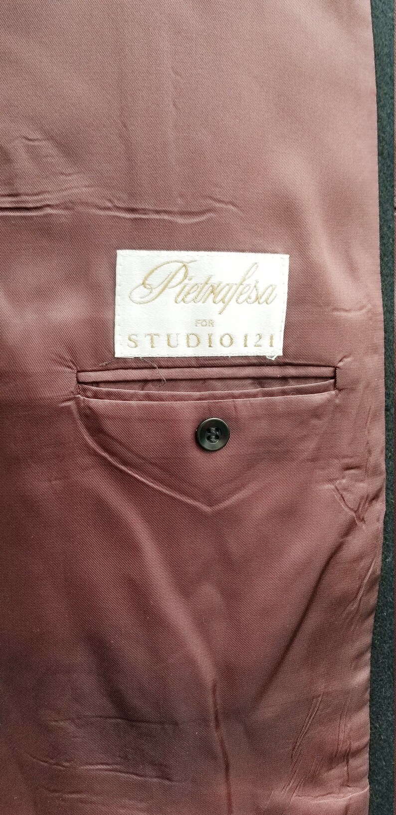 May include: Close-up of the interior of a jacket, featuring a dark burgundy lining. A small pocket is visible, along with a black button. A label reads "Pietrafesa for STUDIO 121".