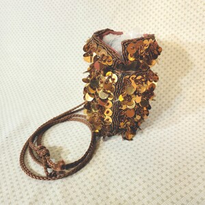 May include: A small, brown drawstring bag with a gold sequin design. The bag has a brown cord attached to it.