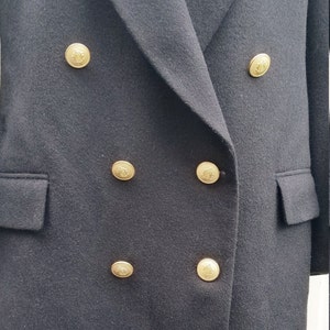 May include: A black double-breasted blazer with gold-colored buttons. The blazer has two front pockets and a notched lapel. The buttons are embossed with a decorative design. The fabric appears to be a wool blend.
