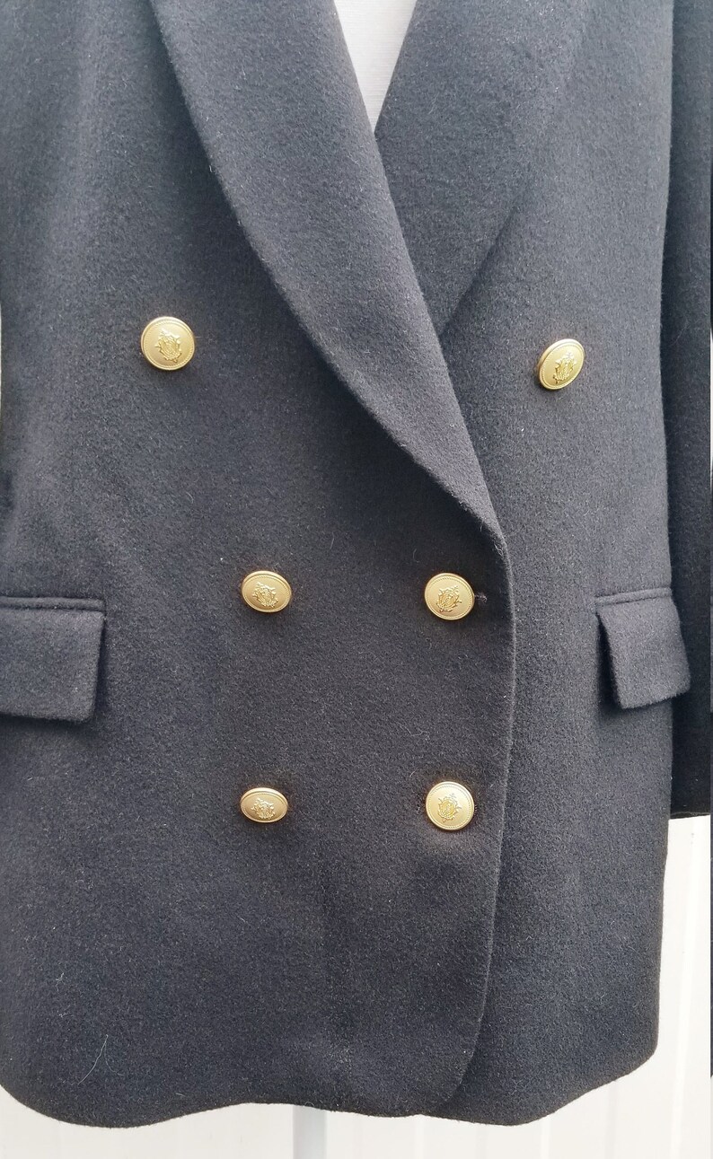 May include: A black double-breasted blazer with gold-colored buttons. The blazer has two front pockets and a notched lapel. The buttons are embossed with a decorative design. The fabric appears to be a wool blend.