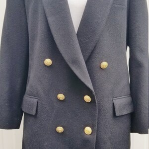 May include: A black double-breasted blazer with gold-colored buttons. The blazer has a notched lapel and two front pockets. The buttons are round with a decorative design. The blazer is displayed on a white mannequin.