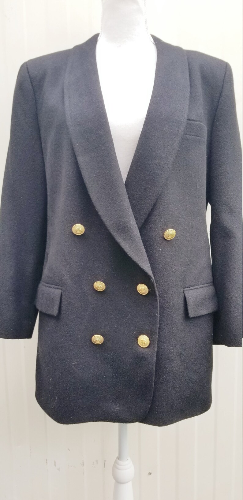 May include: A black double-breasted blazer with gold-colored buttons. The blazer has a notched lapel and two front pockets. The buttons are round with a decorative design. The blazer is displayed on a white mannequin.