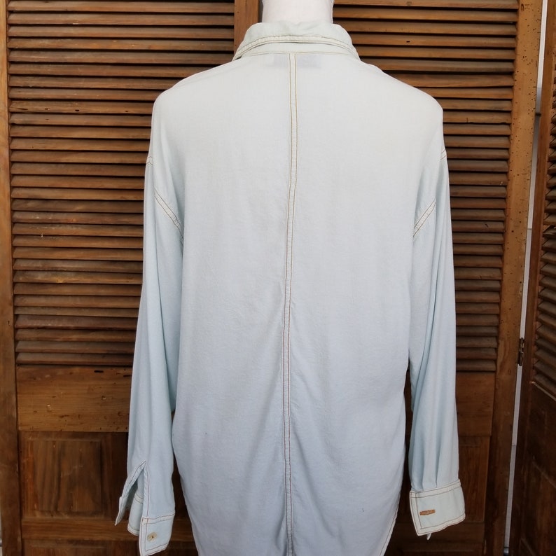 May include: A light blue long-sleeved shirt with a button-up collar and a single seam down the back.