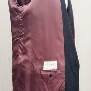 May include: Black blazer with a burgundy satin lining. The interior features a pocket with a button closure and a label that reads "Pietrafesa STUDIO 121". The blazer is displayed on a white mannequin.