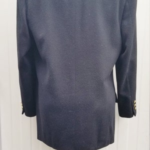 May include: A black blazer with gold buttons on the sleeves. The blazer is displayed on a white mannequin. The back of the blazer is visible, showing the tailored fit and classic design. A timeless piece for any wardrobe.
