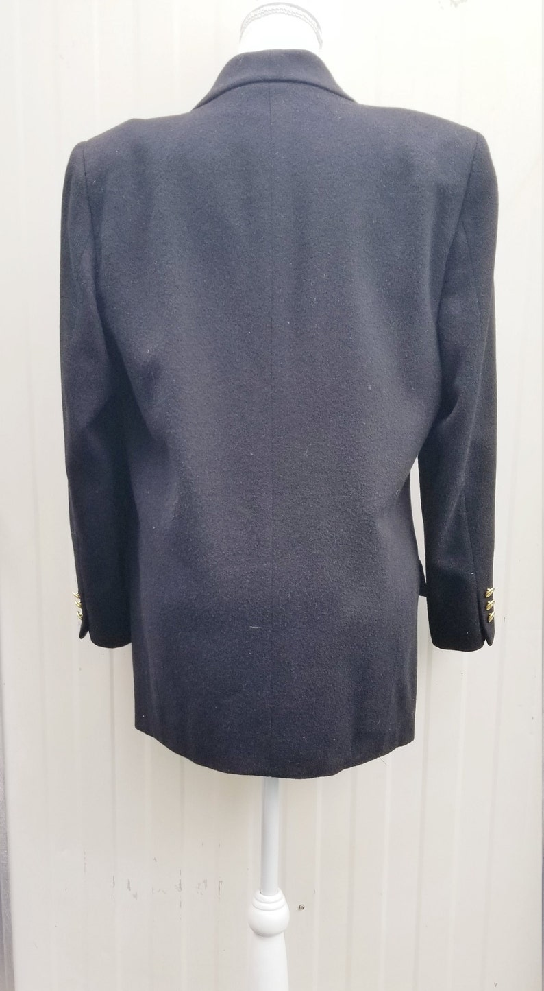 May include: A black blazer with gold buttons on the sleeves. The blazer is displayed on a white mannequin. The back of the blazer is visible, showing the tailored fit and classic design. A timeless piece for any wardrobe.